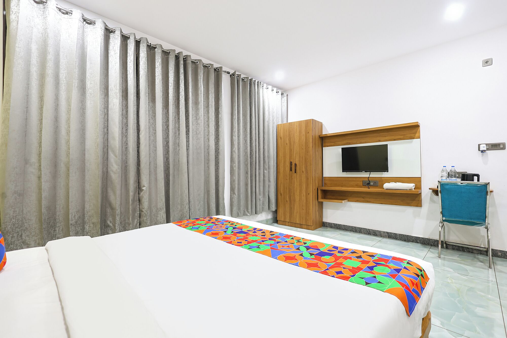 A hotel room with a bed, a TV, a wooden wardrobe, a desk with a chair, and a bathroom.