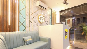 A reception area with a light blue sofa, a reception desk with a logo, and a marble wall with geometric patterns. - Fabhotel Lorven Grand (Visakhapatnam)