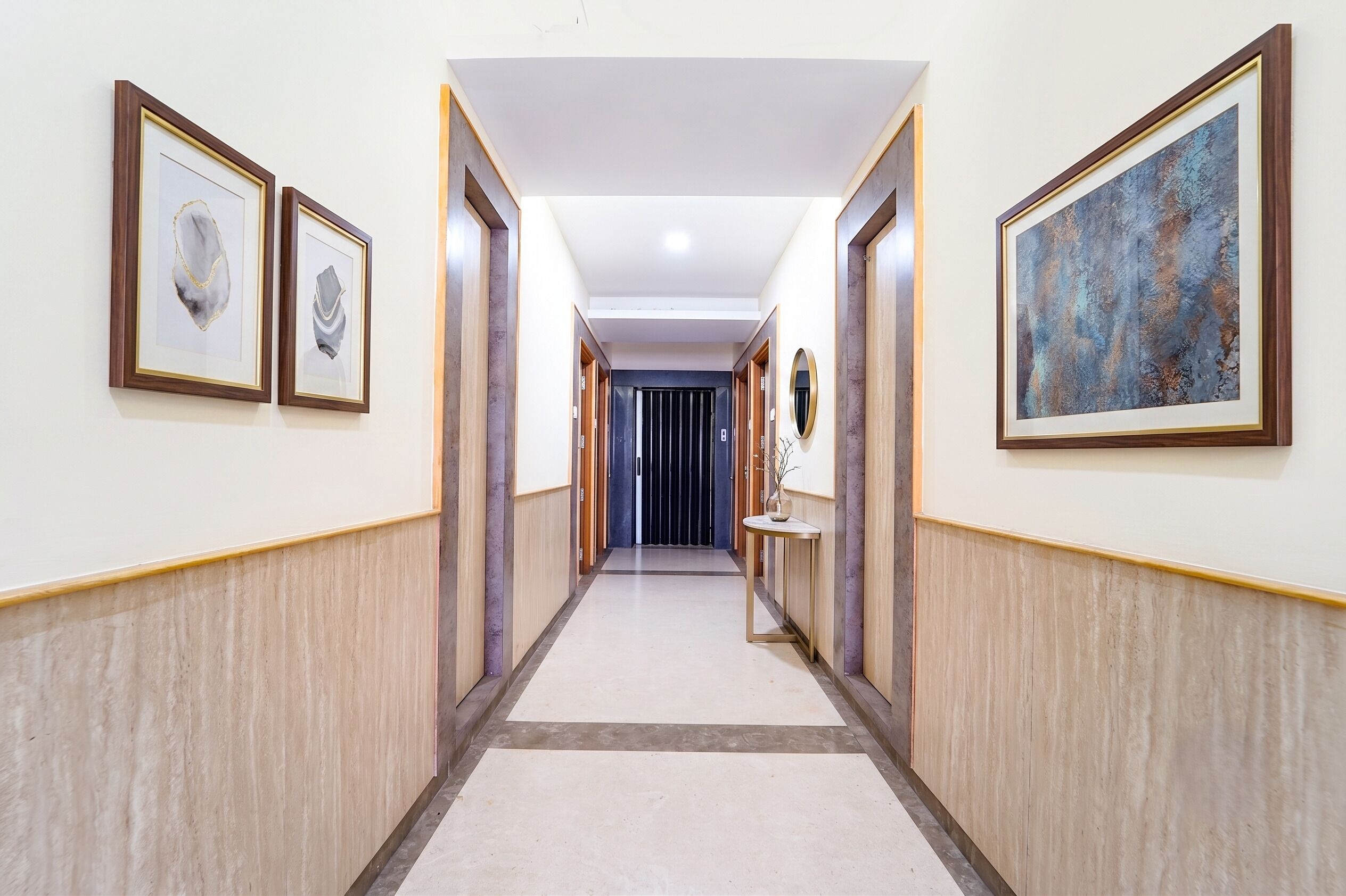 A hotel hallway with framed artwork on the walls, a central light fixture, and a door at the end.