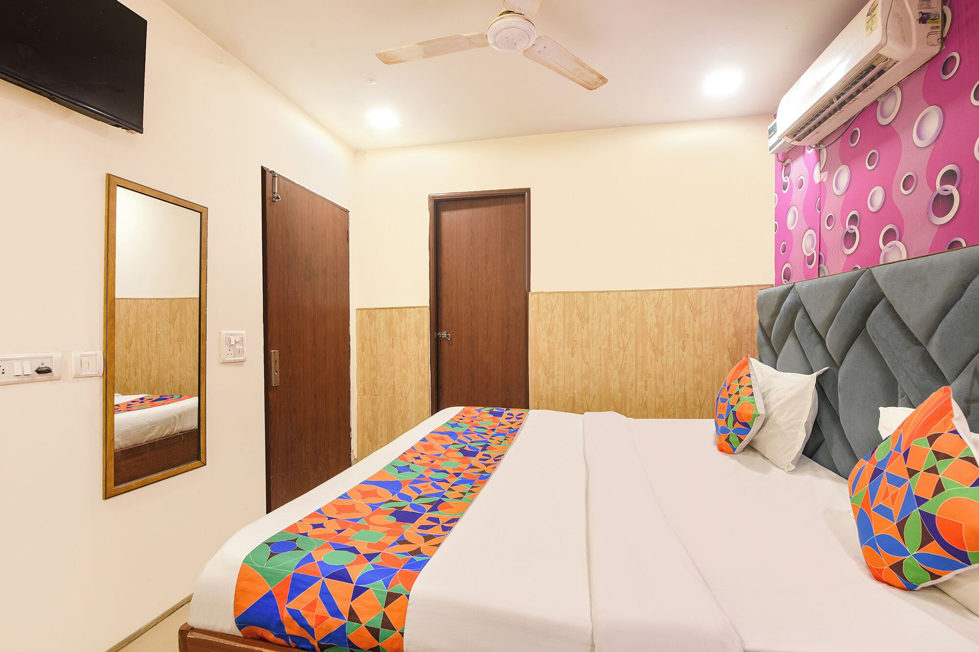 A hotel room with a bed, a ceiling fan, an air conditioning unit, and a mirror.