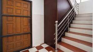 A staircase with a metal handrail and wooden steps, adjacent to a large wooden door with a black frame. - Fabhotel Madras Residency (Chennai)