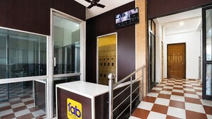 A hotel reception area with a checkered floor, a reception desk with a logo, a television screen, and a staircase. - Fabhotel Madras Residency (Chennai)