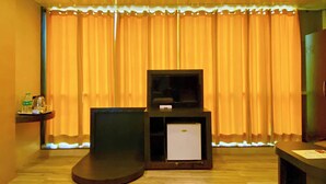 Ein Zimmer mit Fernseher auf einem Schrank, einem kleinen Kühlschrank und einer Wasserflasche auf einem Regal.