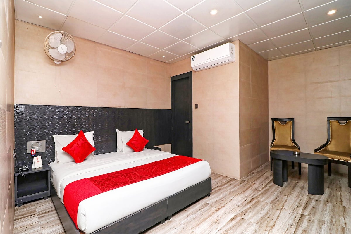 A hotel room with a bed, bedside table, chair, and an air conditioning unit.