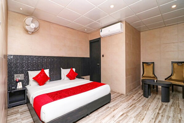 A hotel room with a bed, bedside table, chair, and an air conditioning unit.