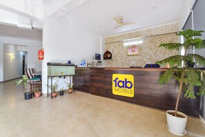 Zona de recepción de hotel con mostrador de madera, un acuario, plantas en macetas y un ventilador de techo.