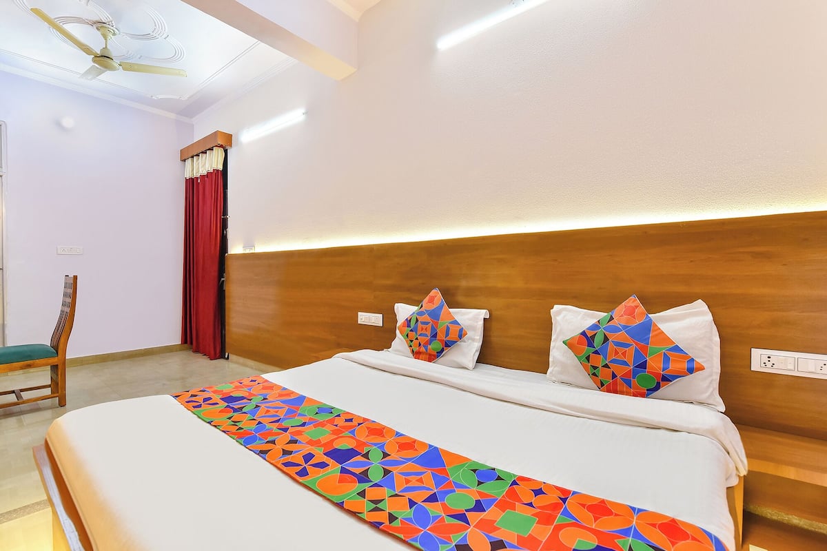 A hotel room with a bed, a chair, a ceiling fan, and a wall-mounted light.