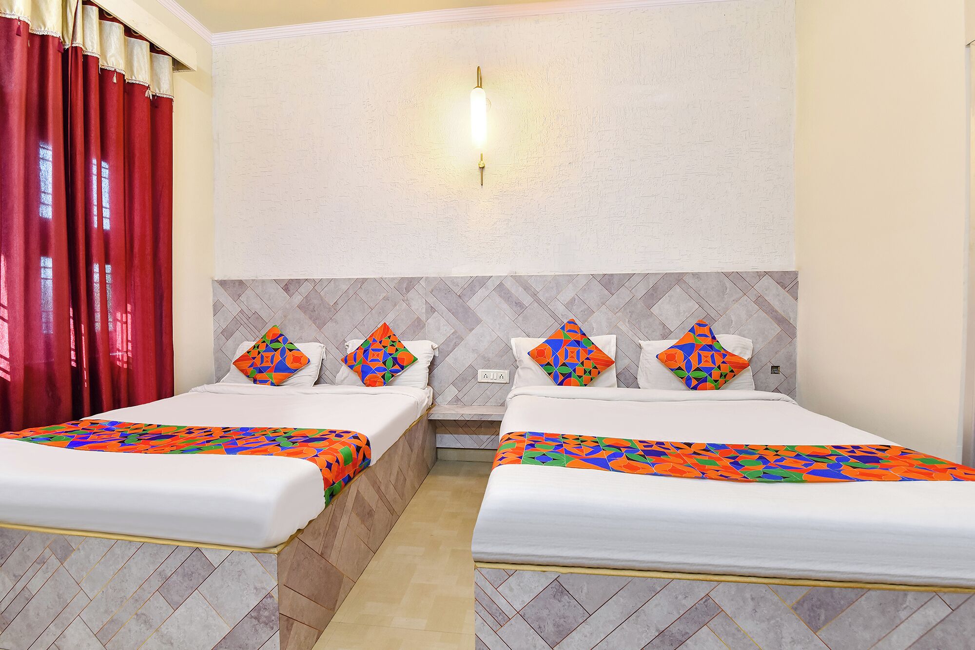 A hotel room with two beds, a red curtain, a patterned wall, and a light fixture.