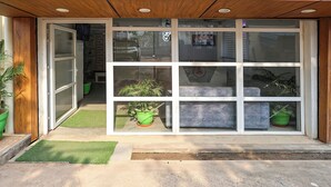 Une entrée d’immeuble avec une porte en verre, des plantes en pot et un petit tapis vert.