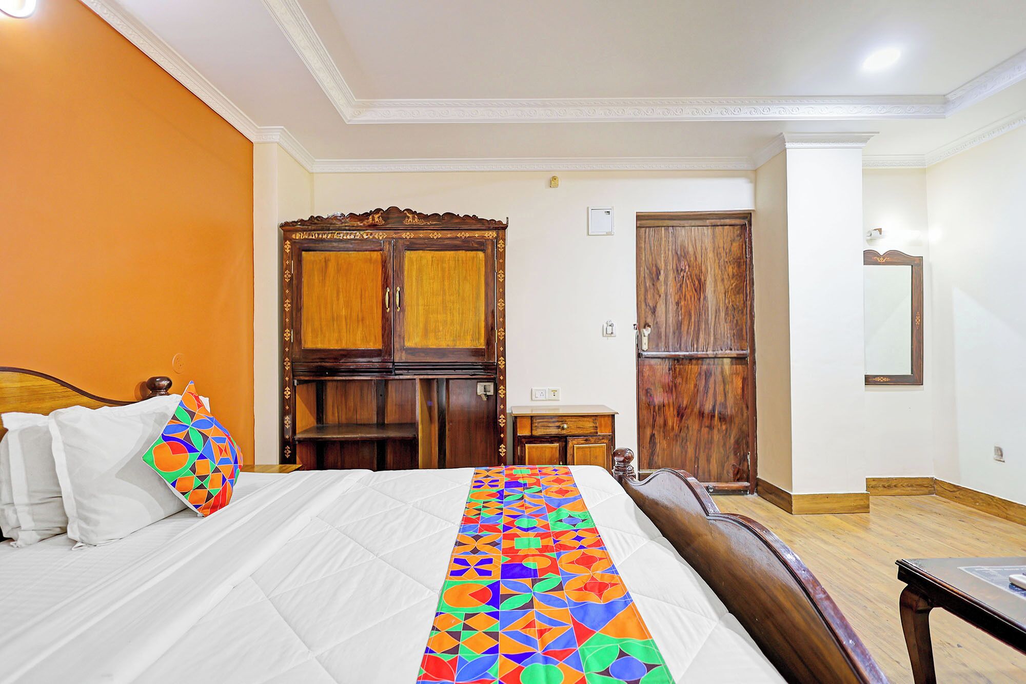 Una habitación de hotel con cama, armario de madera, una mesita y un espejo.