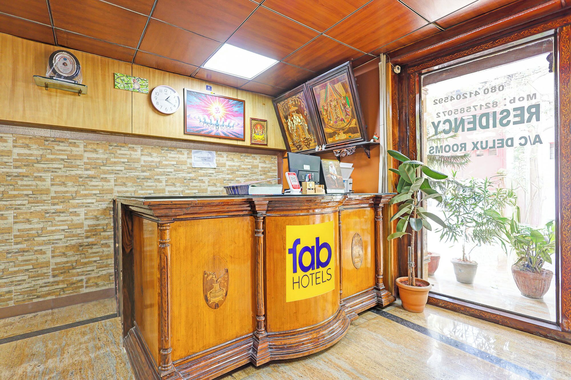 Un comptoir d’accueil avec une enseigne « Tab Hotels », une horloge, un tableau encadré et une fenêtre donnant sur un immeuble.