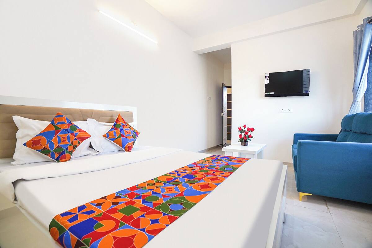 A hotel room with a bed, a TV, a blue armchair, and a small table with flowers.