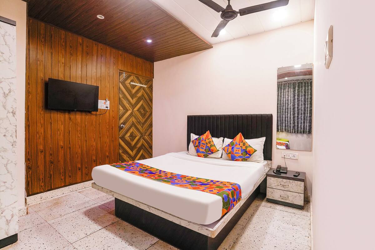Un dormitorio con cama, mesita de noche, televisor y ventilador de techo.