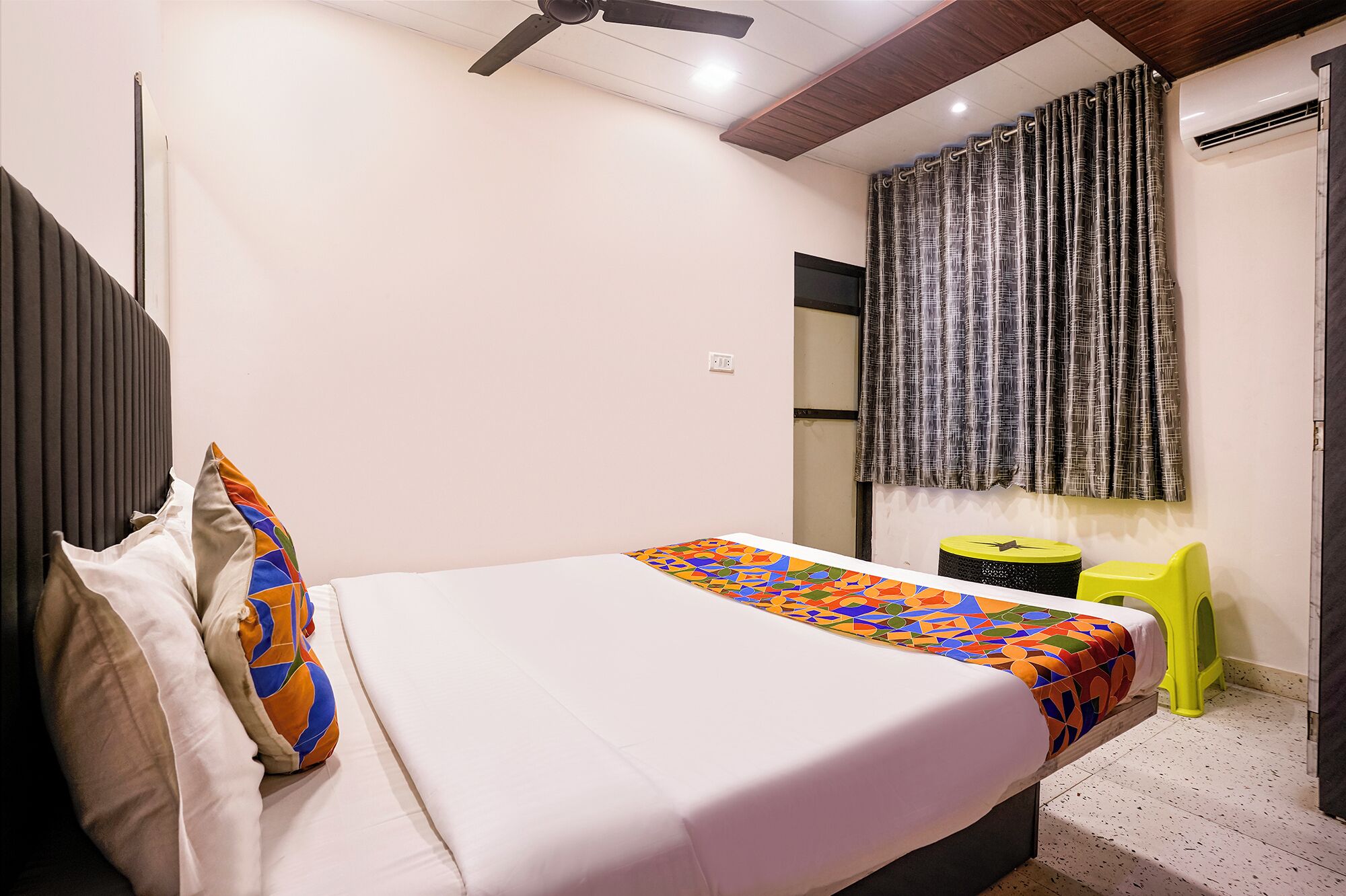 Un dormitorio con cama, ventilador de techo, ventana con cortinas y una pequeña mesa con silla.