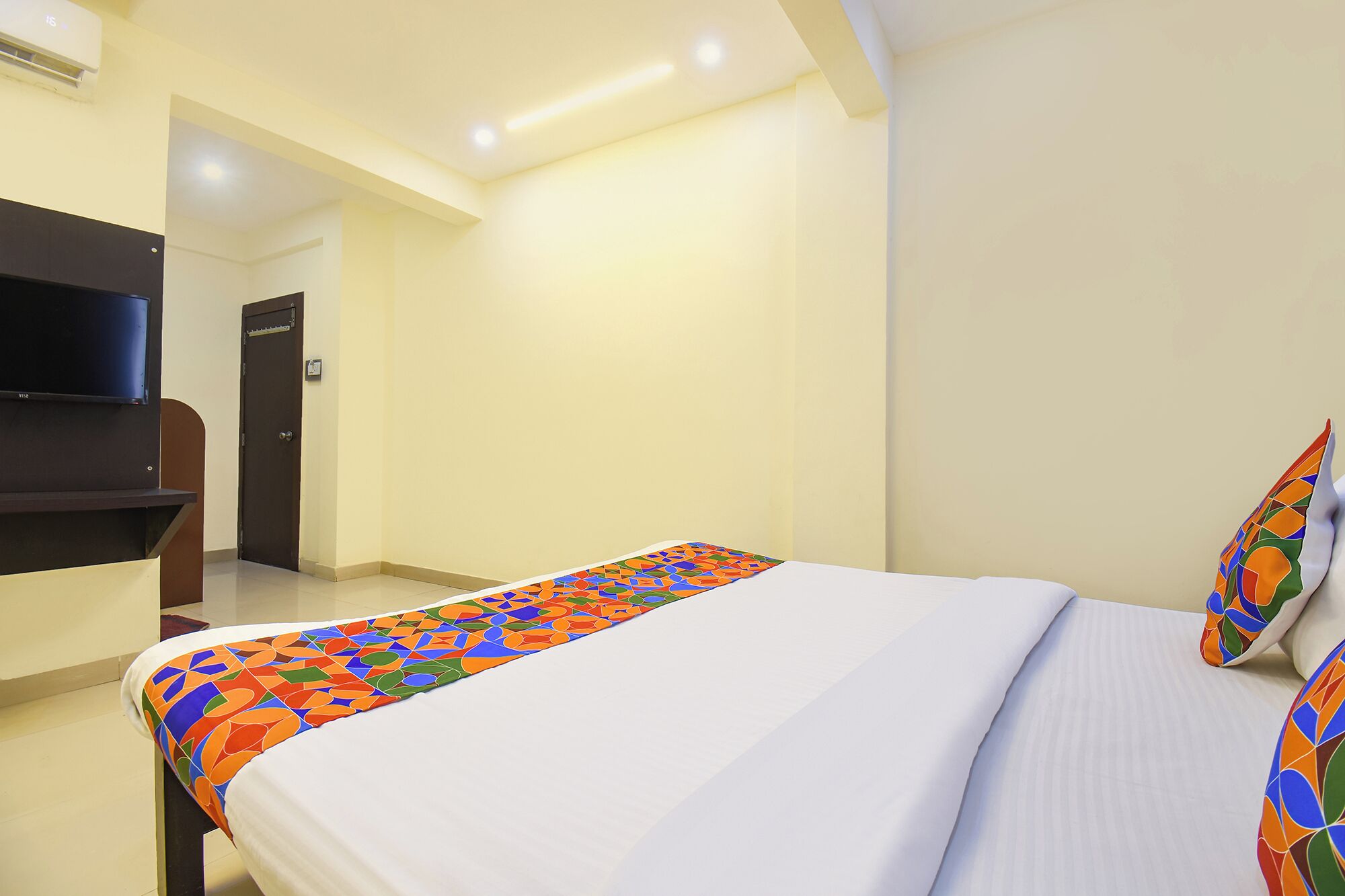 A hotel room with a bed, a TV mounted on the wall, and a door leading to another room.
