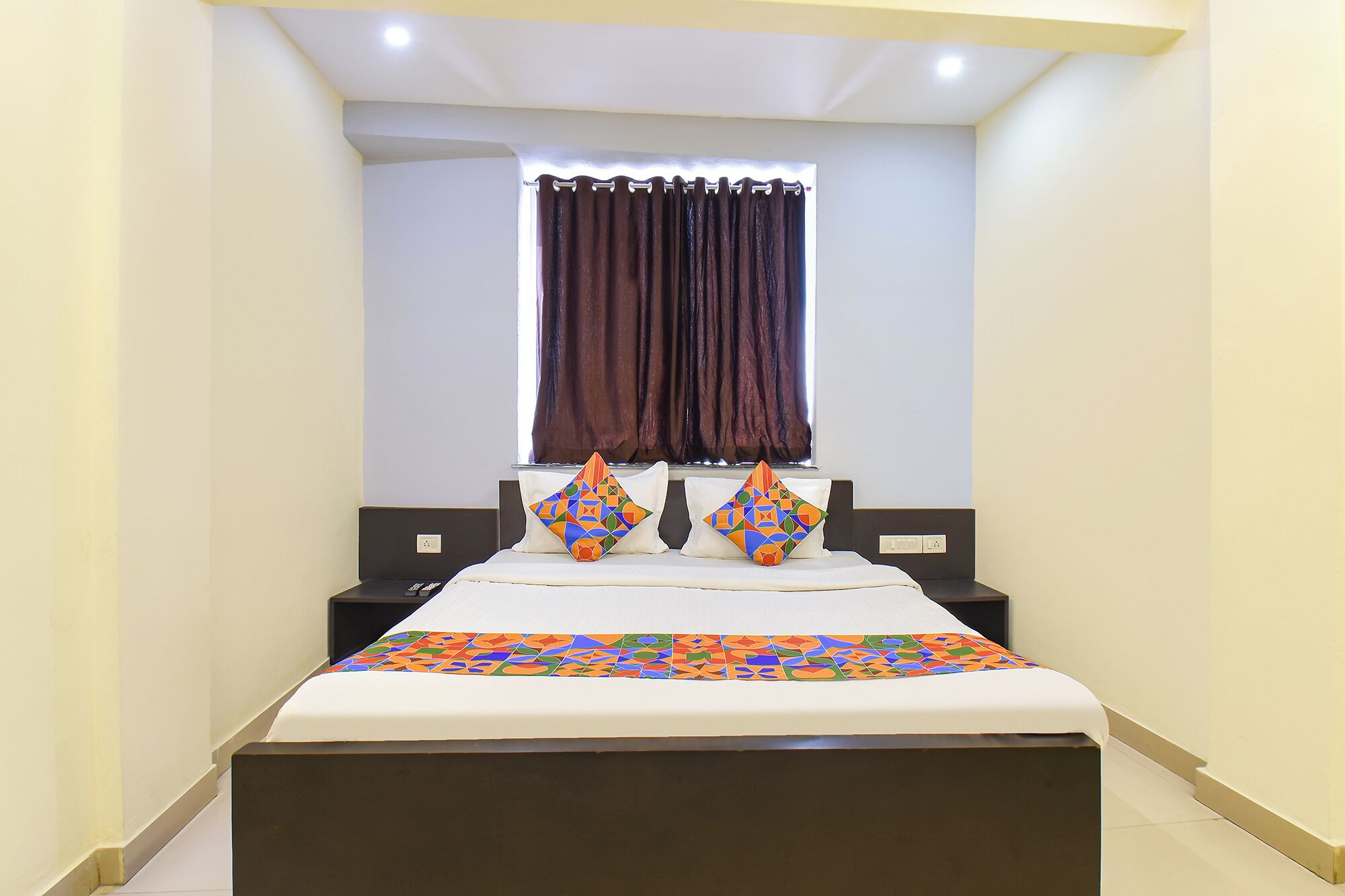 A bedroom with a bed, two nightstands, a window with curtains, and a patterned bedspread.