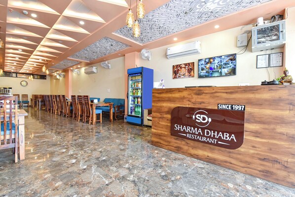 A restaurant interior with a wooden reception desk, seating area, and a blue beverage cooler.