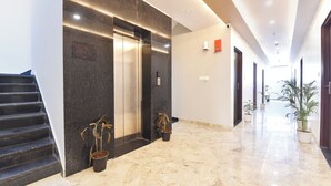 A modern hotel lobby with a marble floor, a staircase, two potted plants, and an elevator. - Fabhotel Dream Stay (Jaipur)
