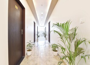 A hallway with a wooden door marked '201', potted plants, and a marble floor.