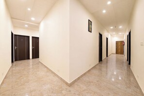 Un largo pasillo bien iluminado con suelo de mármol, varias puertas y un extintor en la pared.