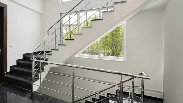 Una escalera moderna con barandillas de metal, escalones de mármol negro y un ventanal con vistas a árboles.