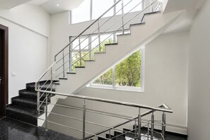 A modern staircase with metal railings, black marble steps, and a large window with a view of trees. - Fabhotel Durga Luxury Studio (Gurugram)