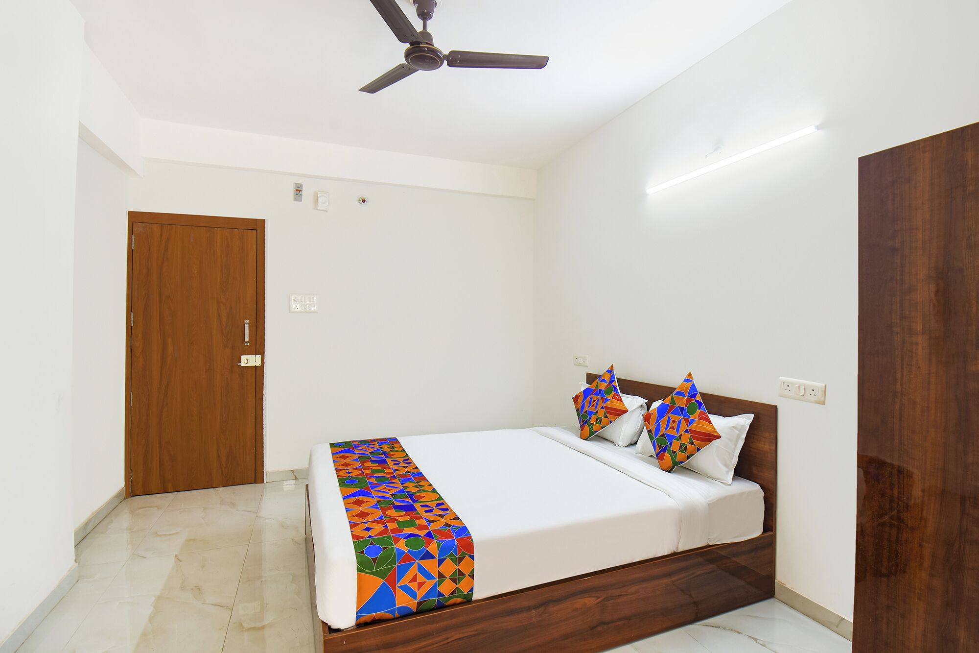 A bedroom with a bed, a ceiling fan, a wooden wardrobe, and a door.