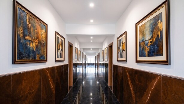 A hallway with framed artwork on the walls, a polished marble floor, and a ceiling with recessed lighting. - Fabhotel Destiny Living (Pune)