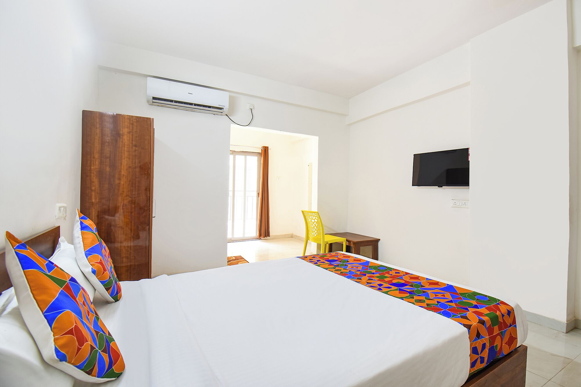 Hotellihuone, jossa on sänky, tuoli, televisio ja ilmastointilaite.
