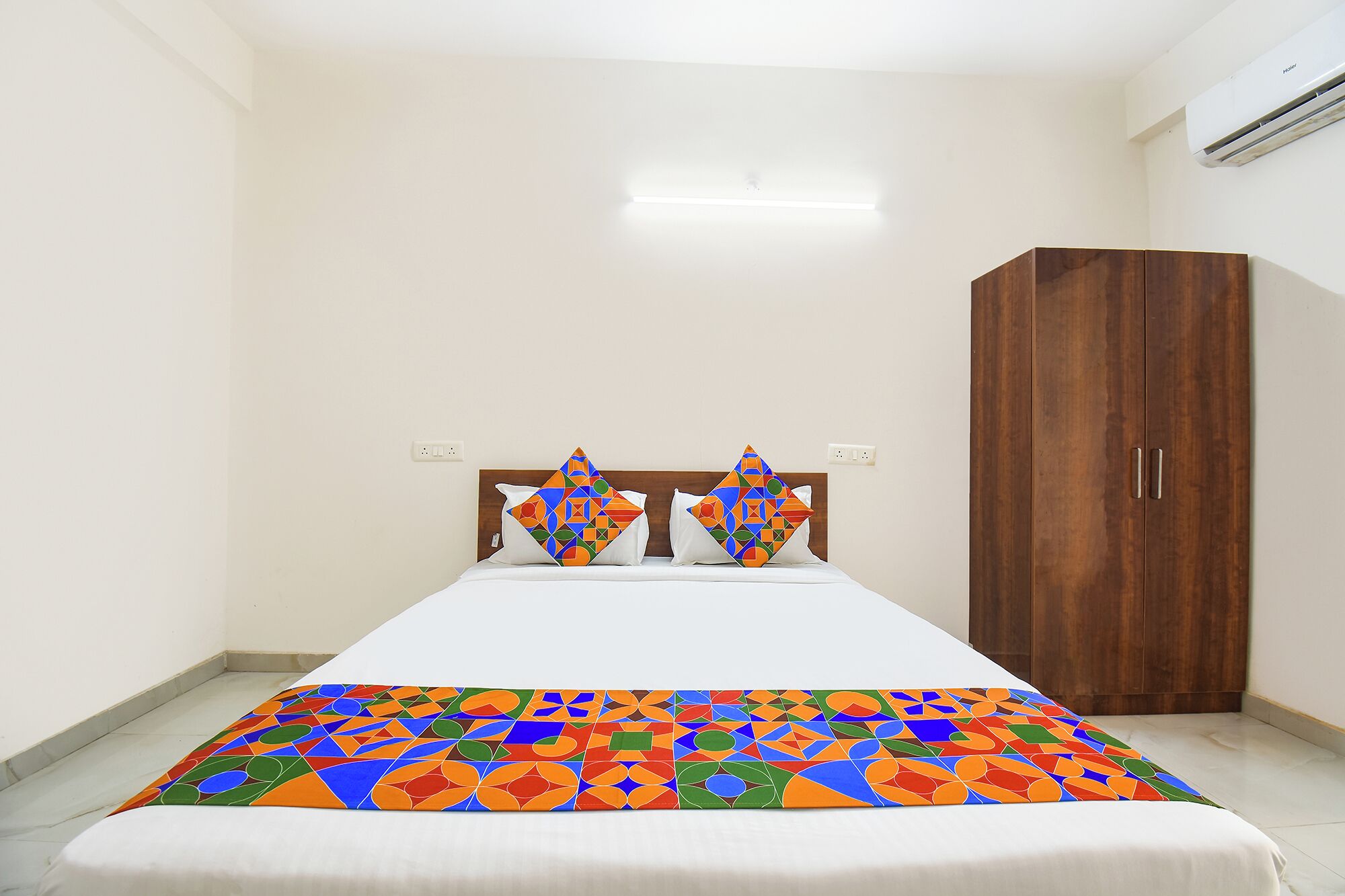 A hotel room with a bed, two pillows, a wooden wardrobe, and a ceiling light.