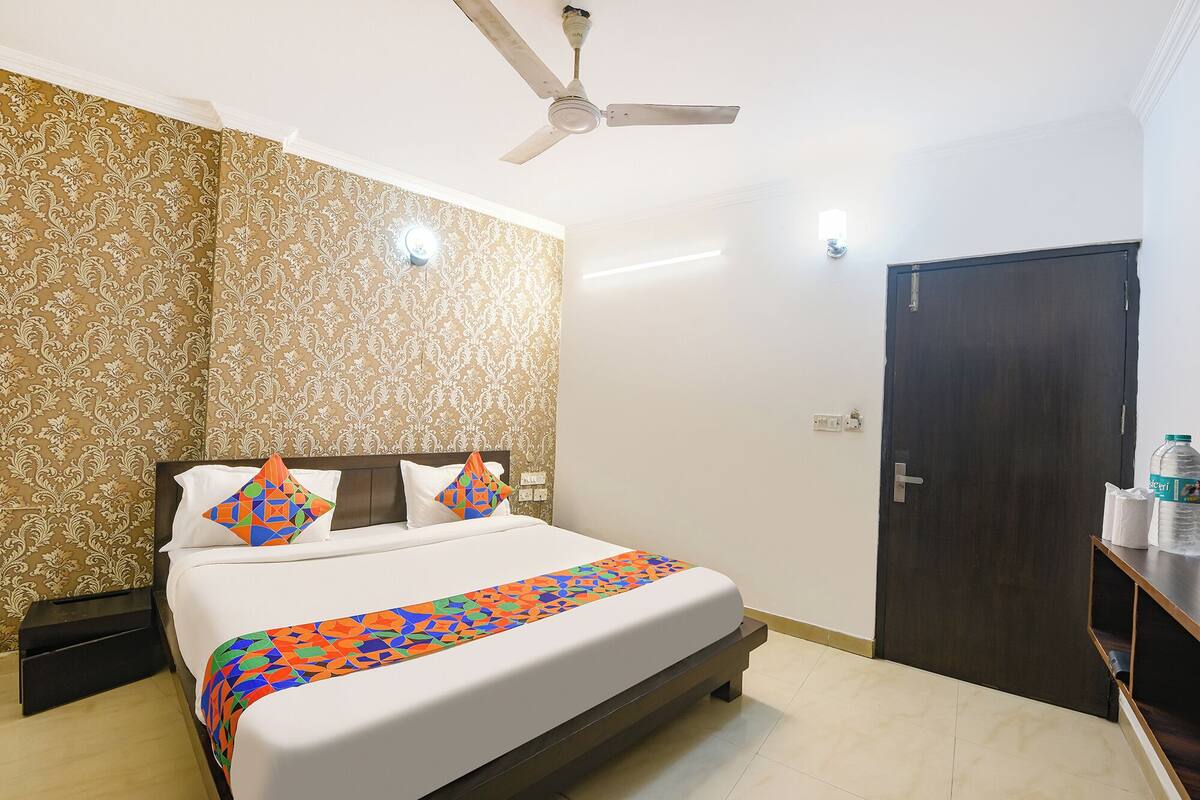 A hotel room with a bed, a ceiling fan, a door, and a wall with patterned wallpaper.