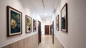 A hallway with framed artwork on the walls, a tiled floor, and doors leading to rooms. - Fabhotel The Max (Lucknow)