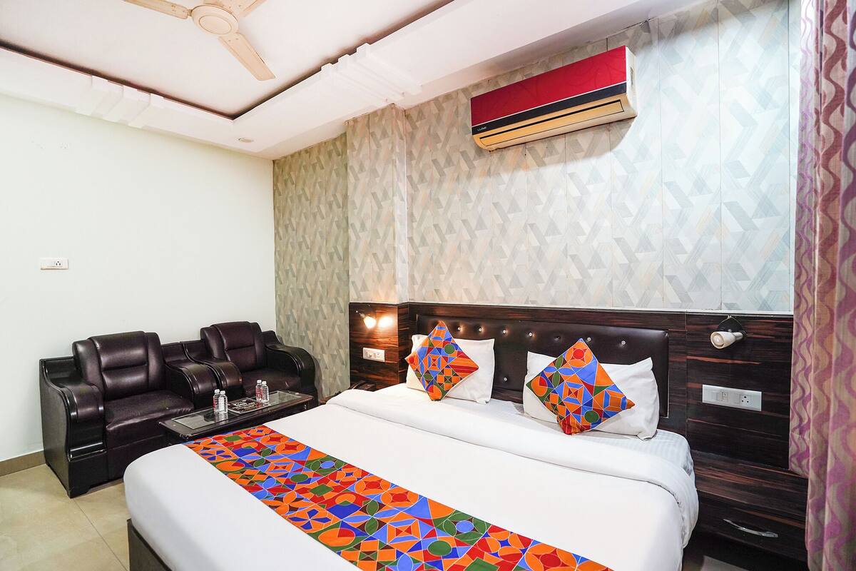 A hotel room with a bed, a massage chair, a wall-mounted air conditioner, and a patterned wall.
