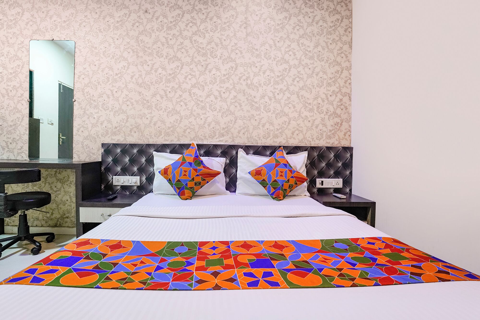 A hotel room with a bed, two nightstands, a mirror, and a desk with a chair.