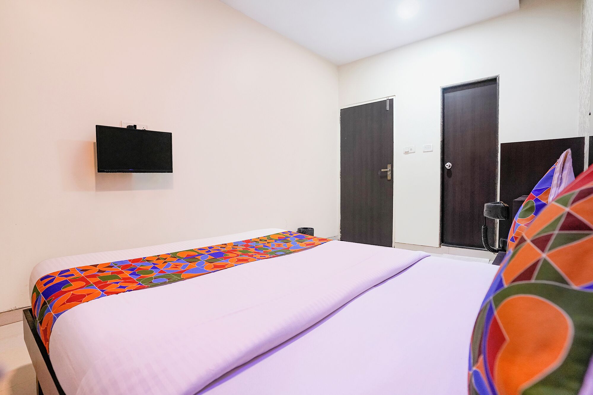A bedroom with a bed, a TV mounted on the wall, and two doors.