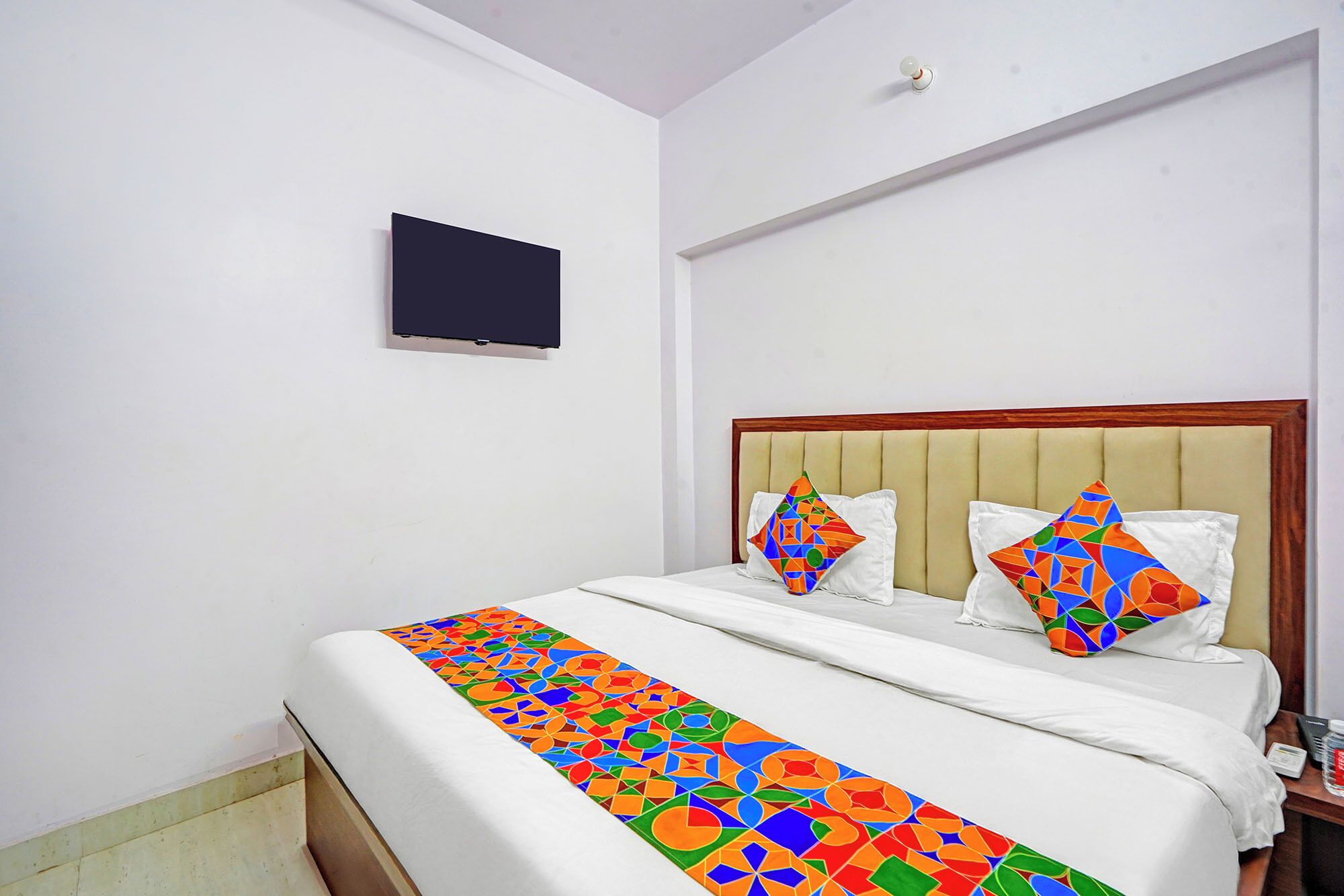 A hotel room with a bed, a television mounted on the wall, and a nightstand with a bottle and a remote control.