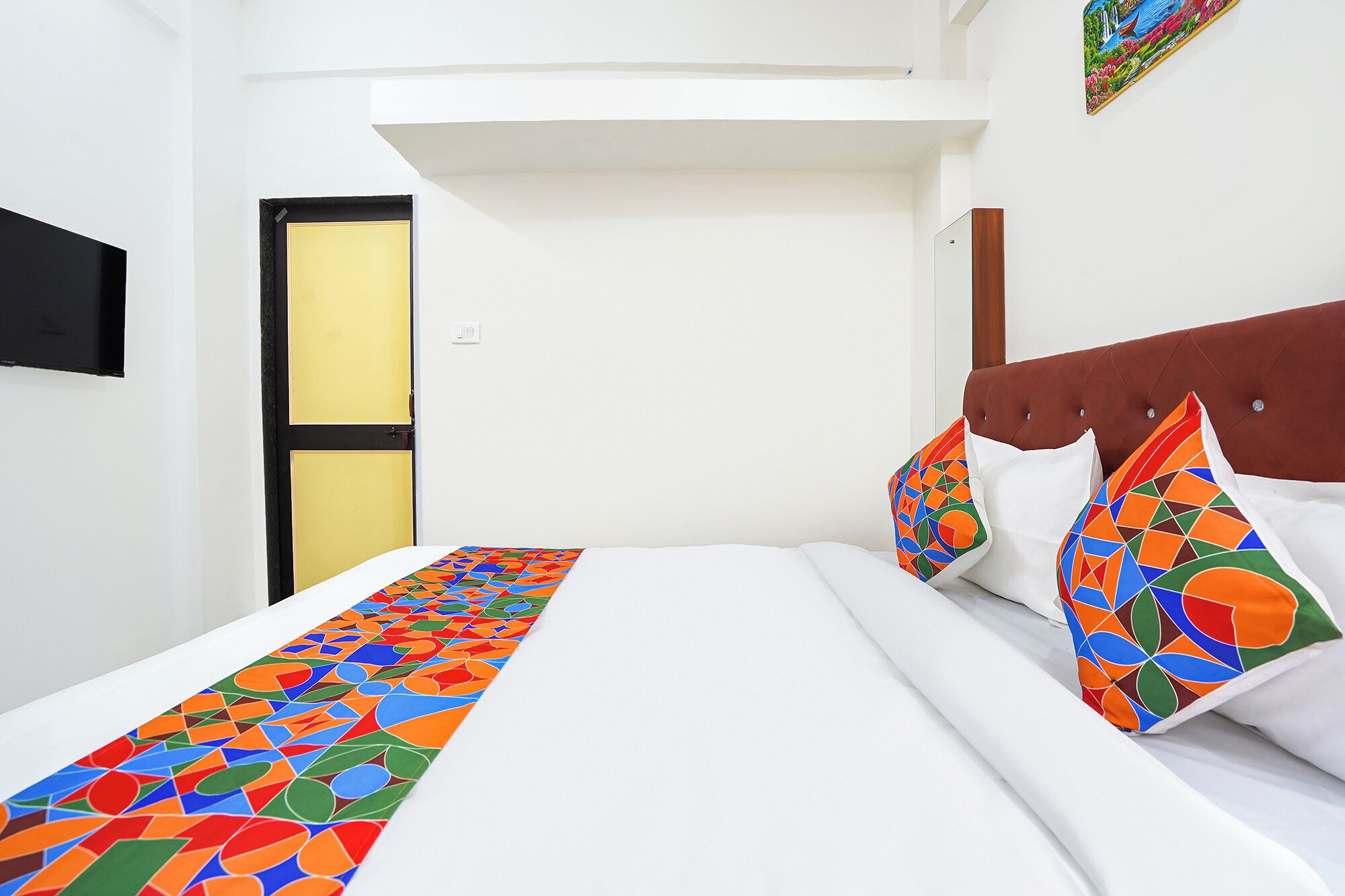 A hotel room with a bed, a headboard, a door, and a wall with a picture.