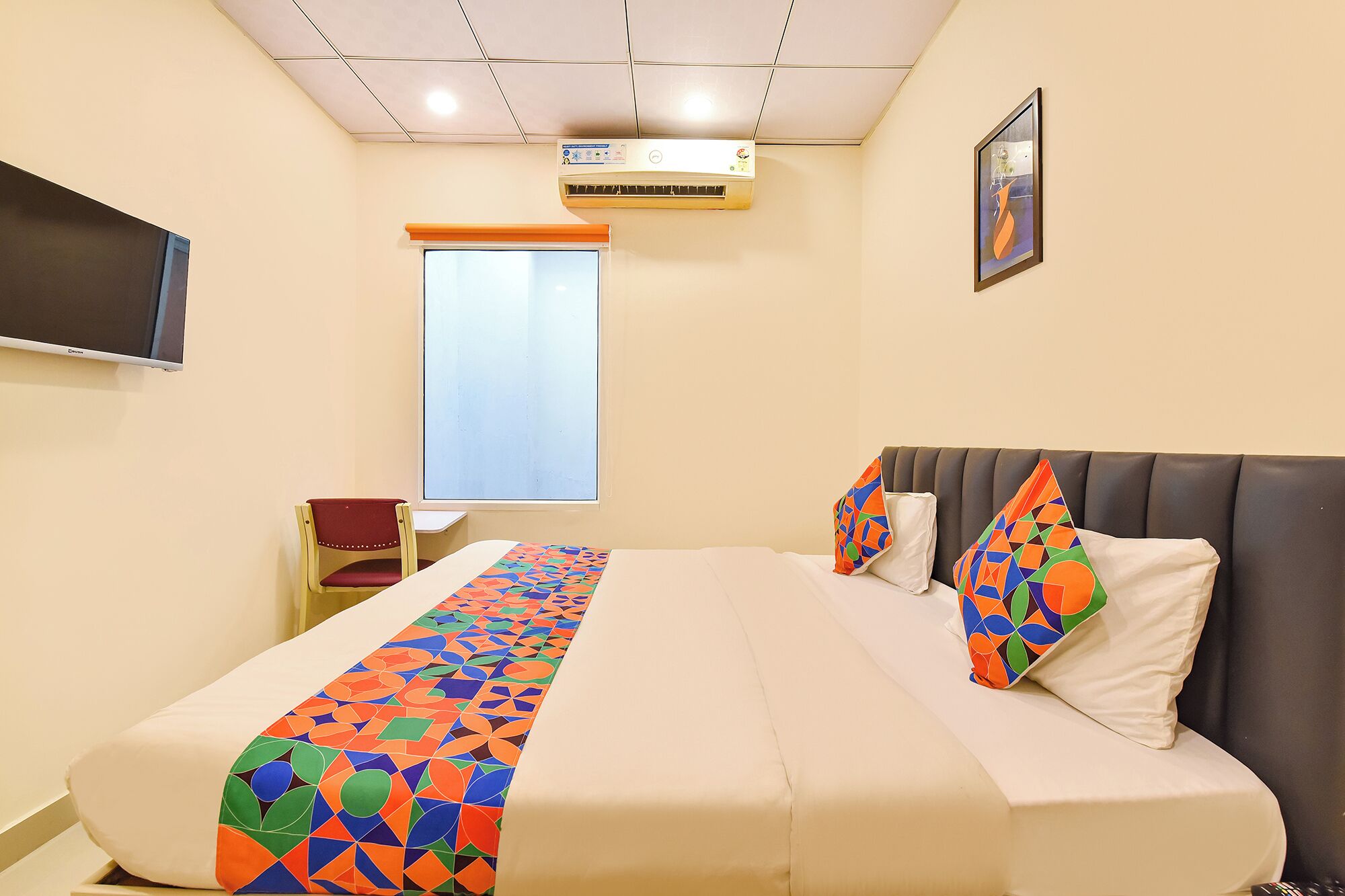 A hotel room with a bed, a TV, an air conditioner, and a window.