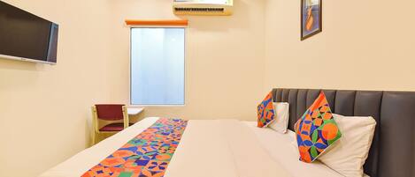 A hotel room with a bed, a TV, an air conditioner, and a window.
