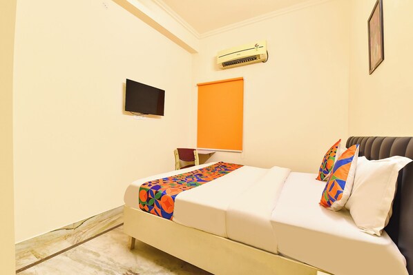 A hotel room with a bed, an air conditioner, a television, and a window with an orange blind. - Fabhotel Mansarovar Retreat (Jaipur)