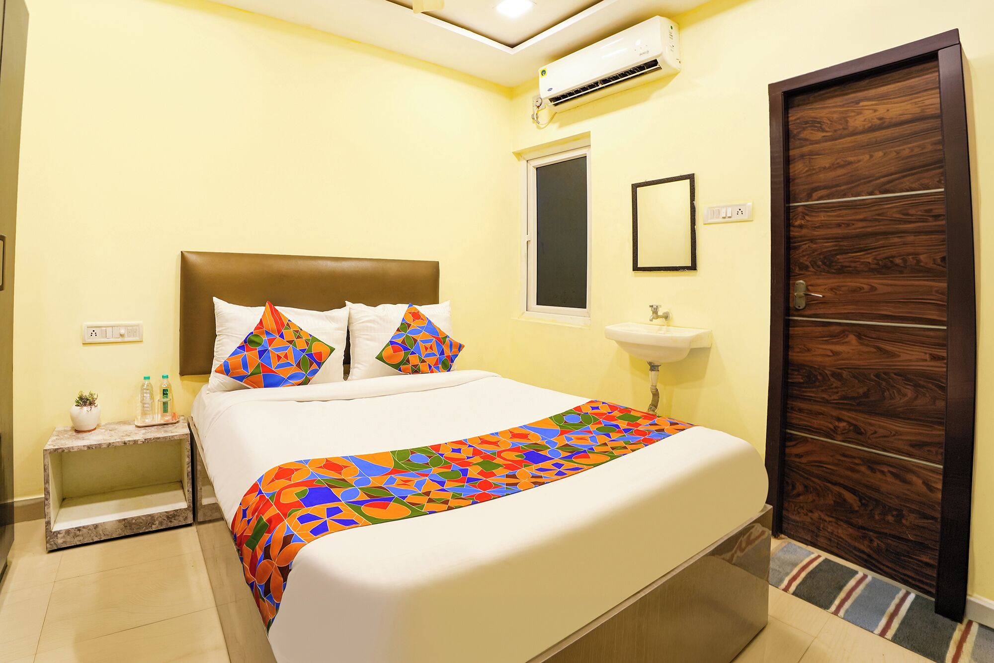 Une chambre d’hôtel comprenant un lit, une table de chevet, un appareil de climatisation, une fenêtre et une porte en bois.