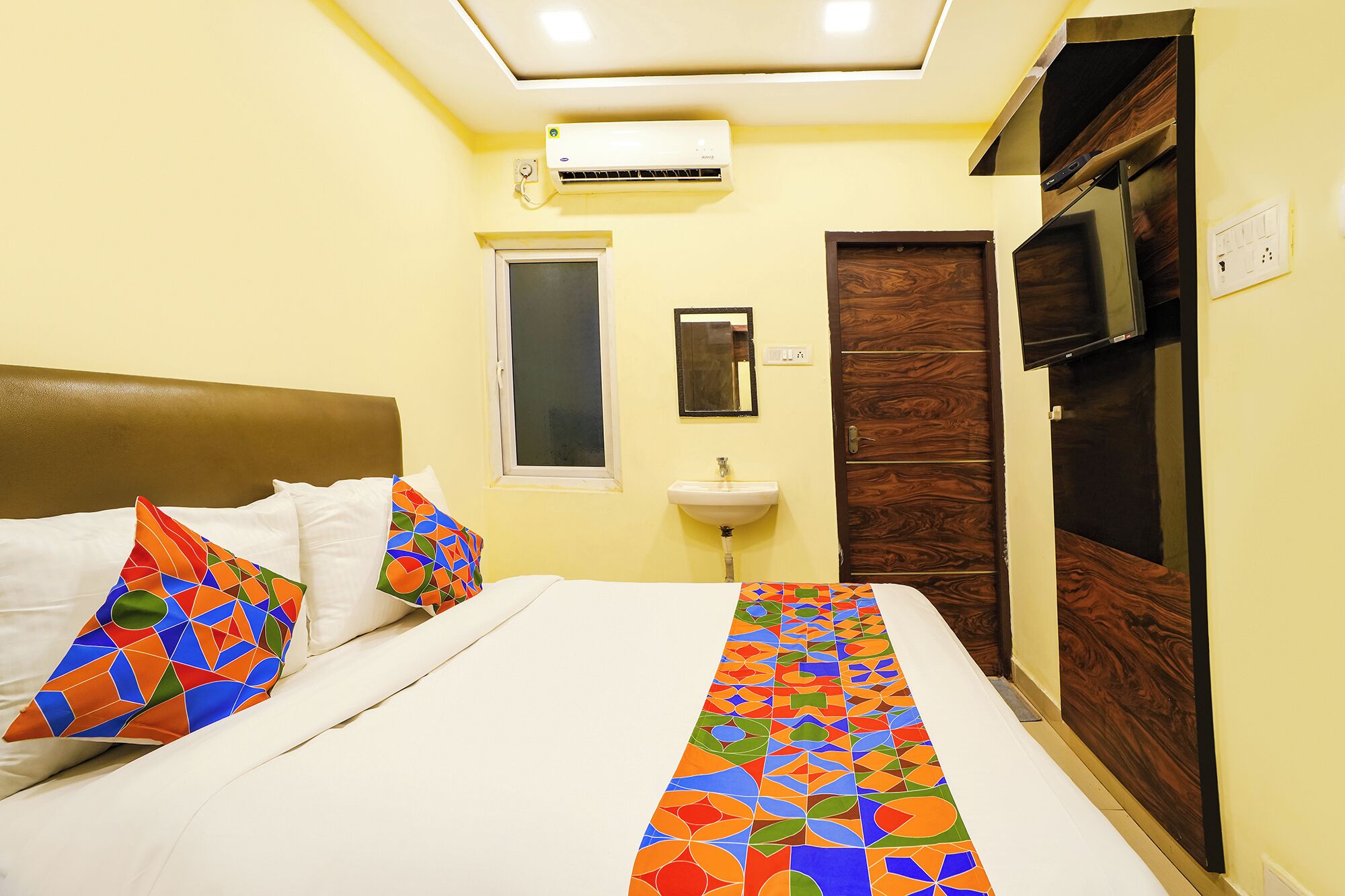 A hotel room with a bed, a window, a sink, and a television.