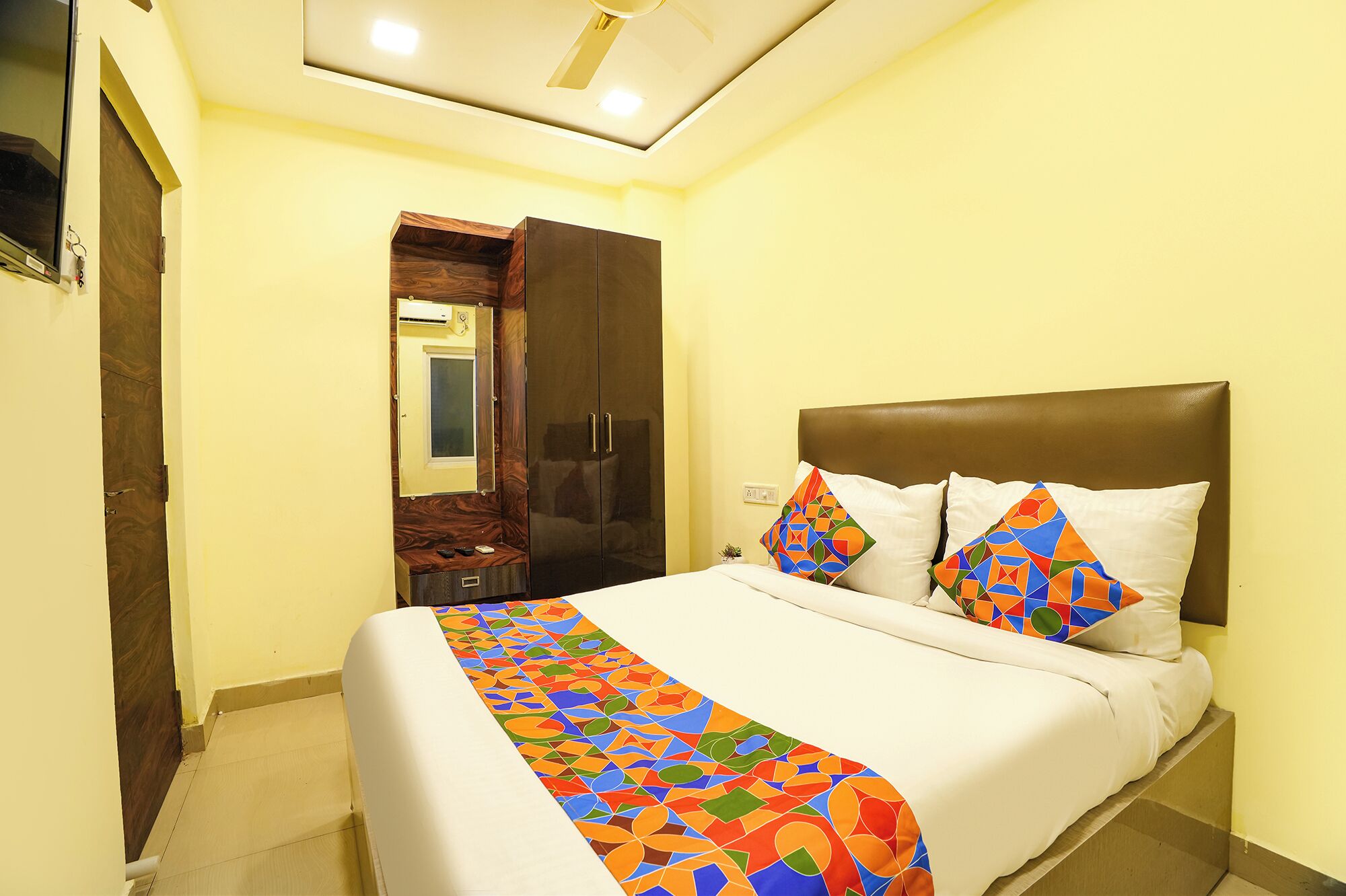 A hotel room with a bed, a wardrobe, a mirror, and a ceiling fan.