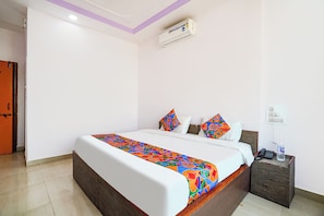 A hotel room with a bed, a nightstand, an air conditioning unit, and a wall socket. - Fabhotel Fortune Inn (Pune)