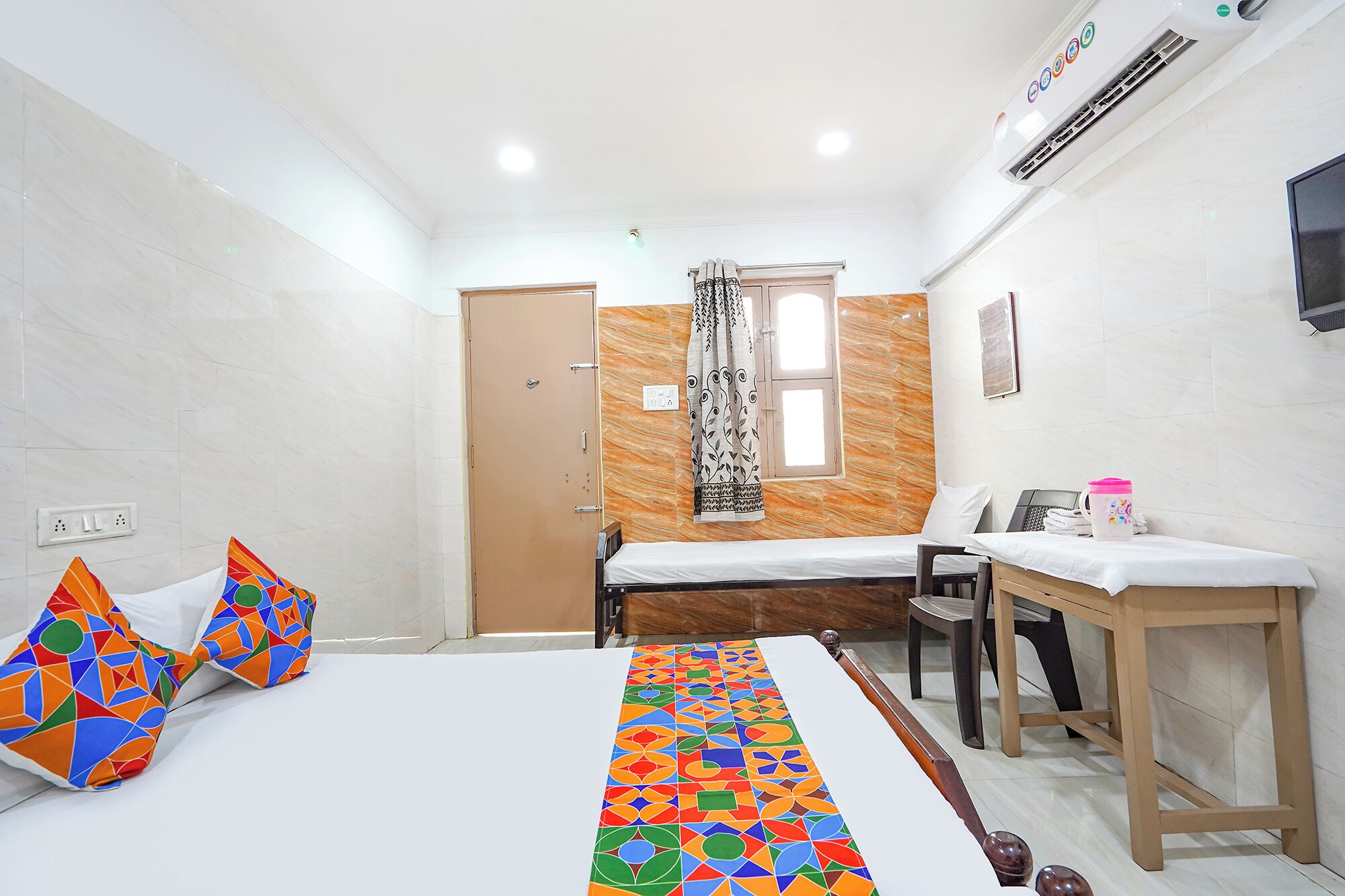 Hotelkamer met een bed, bureau, stoel, raam met gordijnen, televisie en airconditioning.