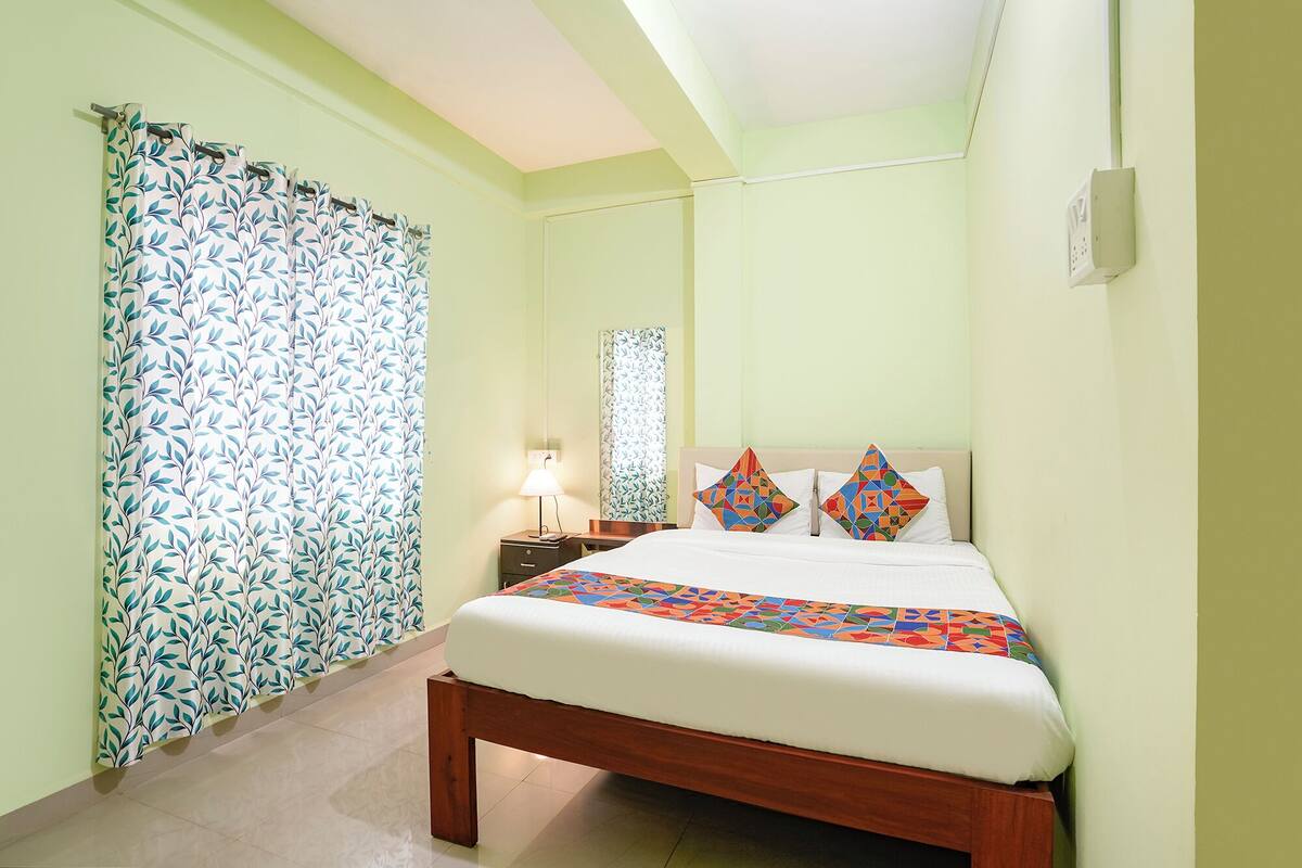 Un dormitorio con cama, mesita de noche, lámpara, espejo y ventana con cortinas.