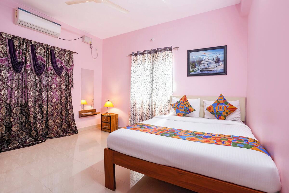 Un dormitorio con temática rosa, que incluye una cama, dos lámparas de noche, una mesita auxiliar, un espejo y un cuadro en la pared.