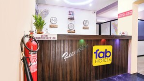 A reception desk with a sign for Fab Hotels, a fire extinguisher, clocks with city names, and a plant. - Fabhotel Shadowline (Panaji)
