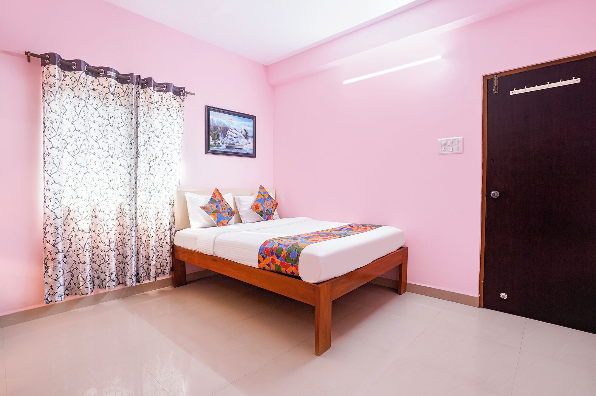 A bedroom with a bed, curtains, a framed picture, and a door.