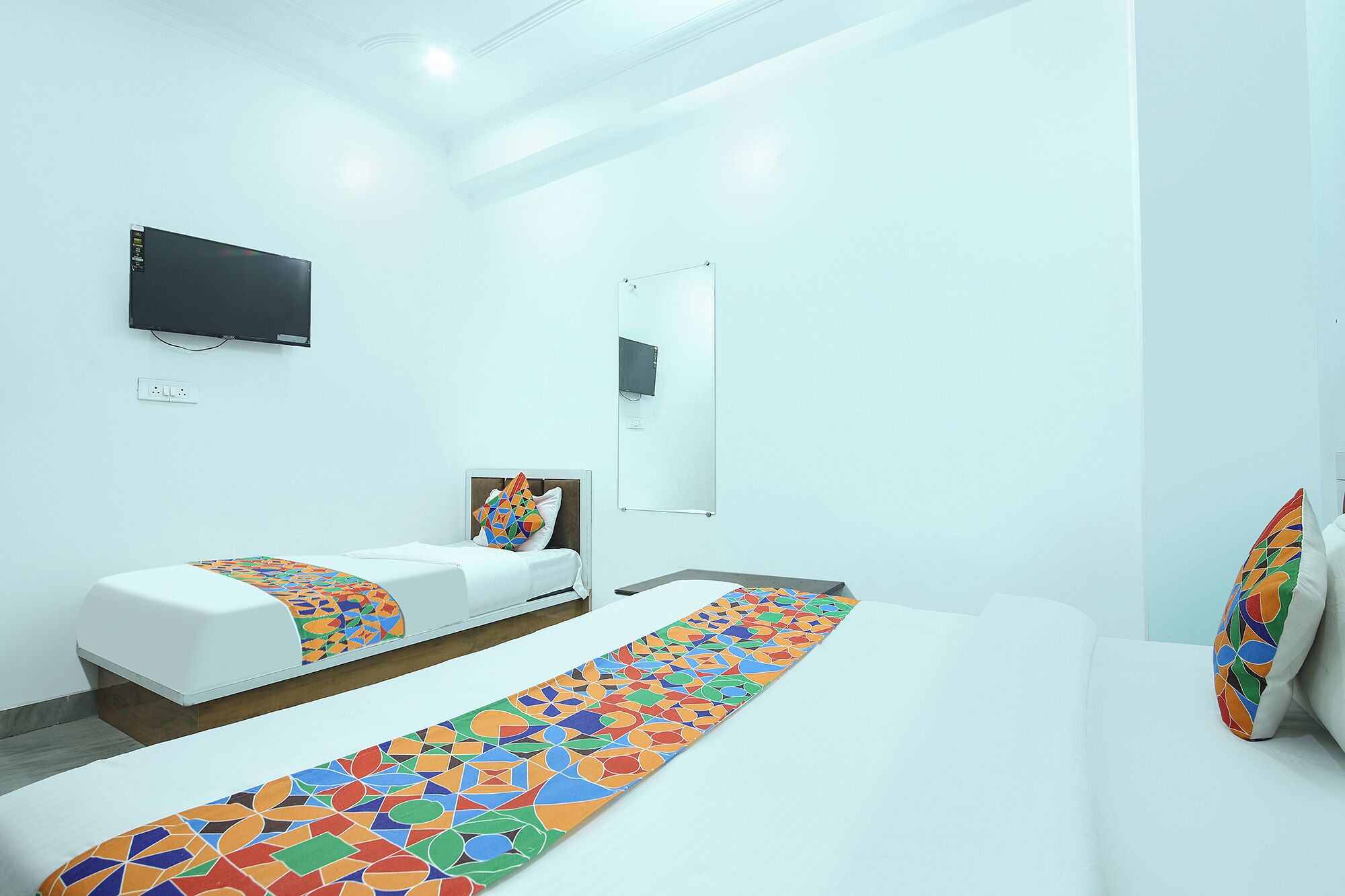 A modern hotel room with a large bed, a smaller bed, a TV, a mirror, and a colorful runner.